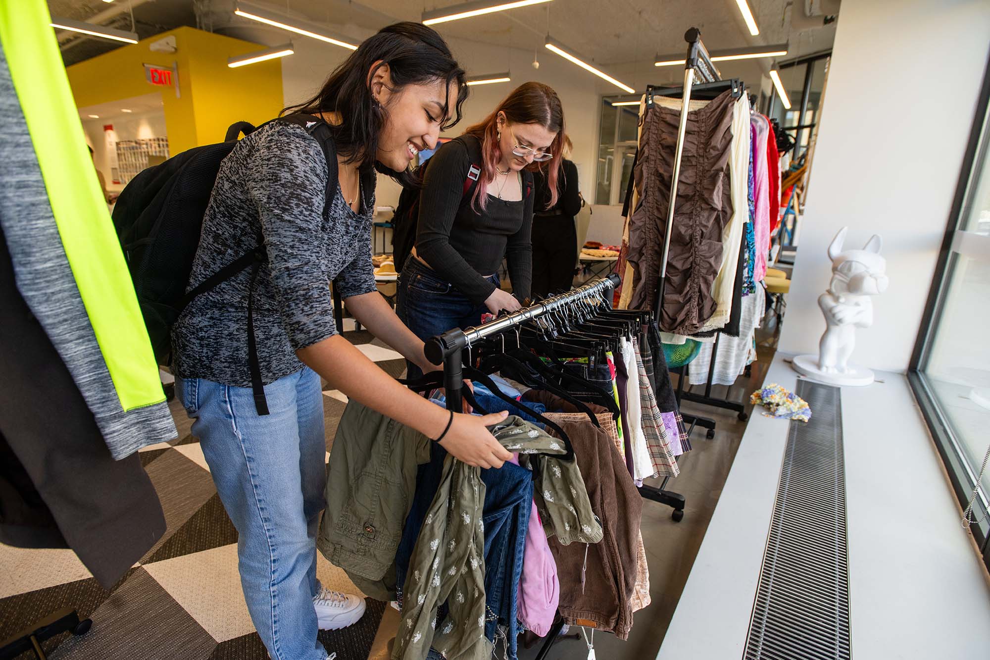 Photo: Two young women are shown browsing through racks of clothing set up in a bright area of the BU Build Lab.