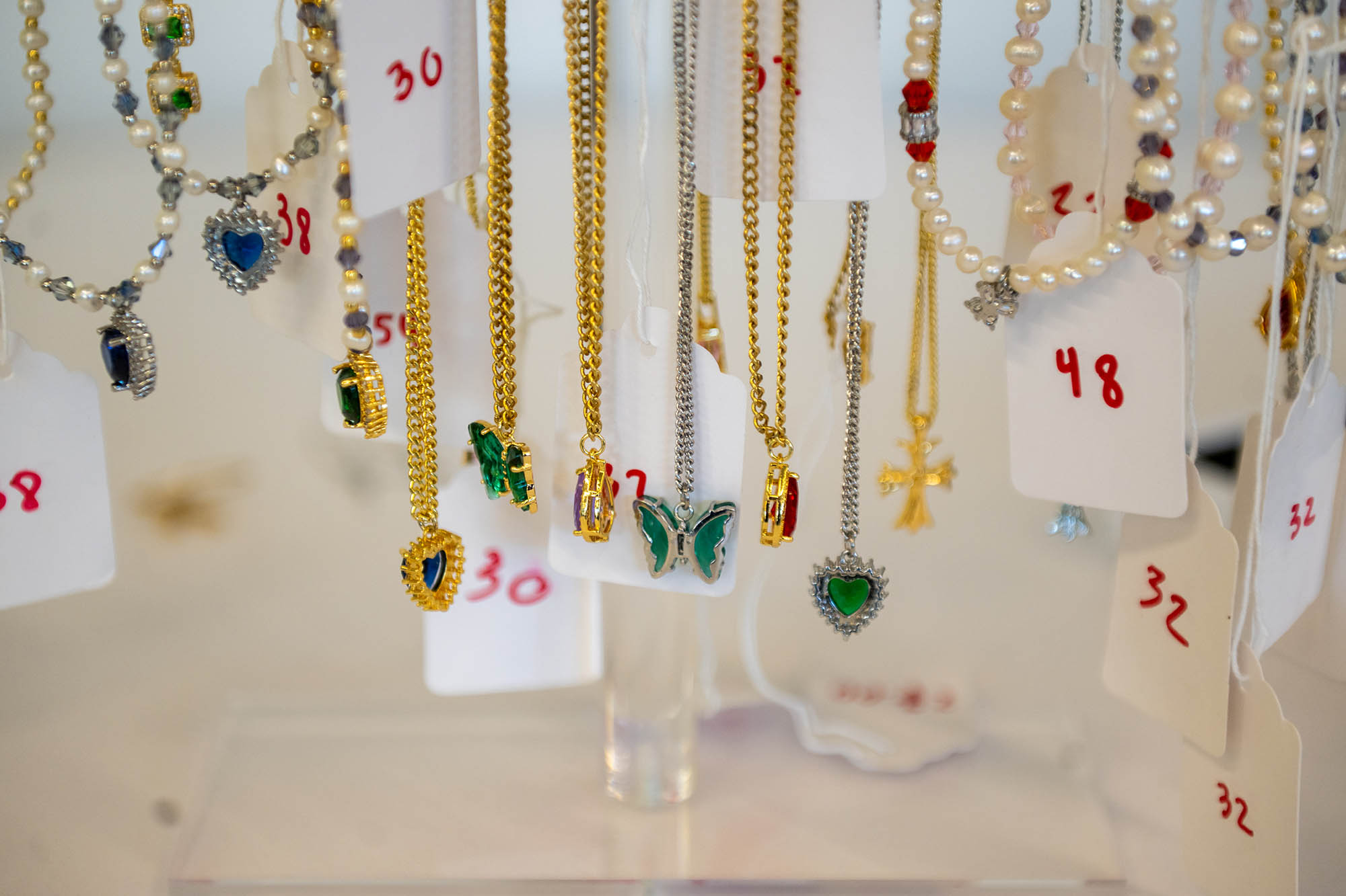 Photo: An assortment of butterfly, heart, and pearl-themed necklaces are shown on display. small, white price tags can be seen hanging from each necklace.