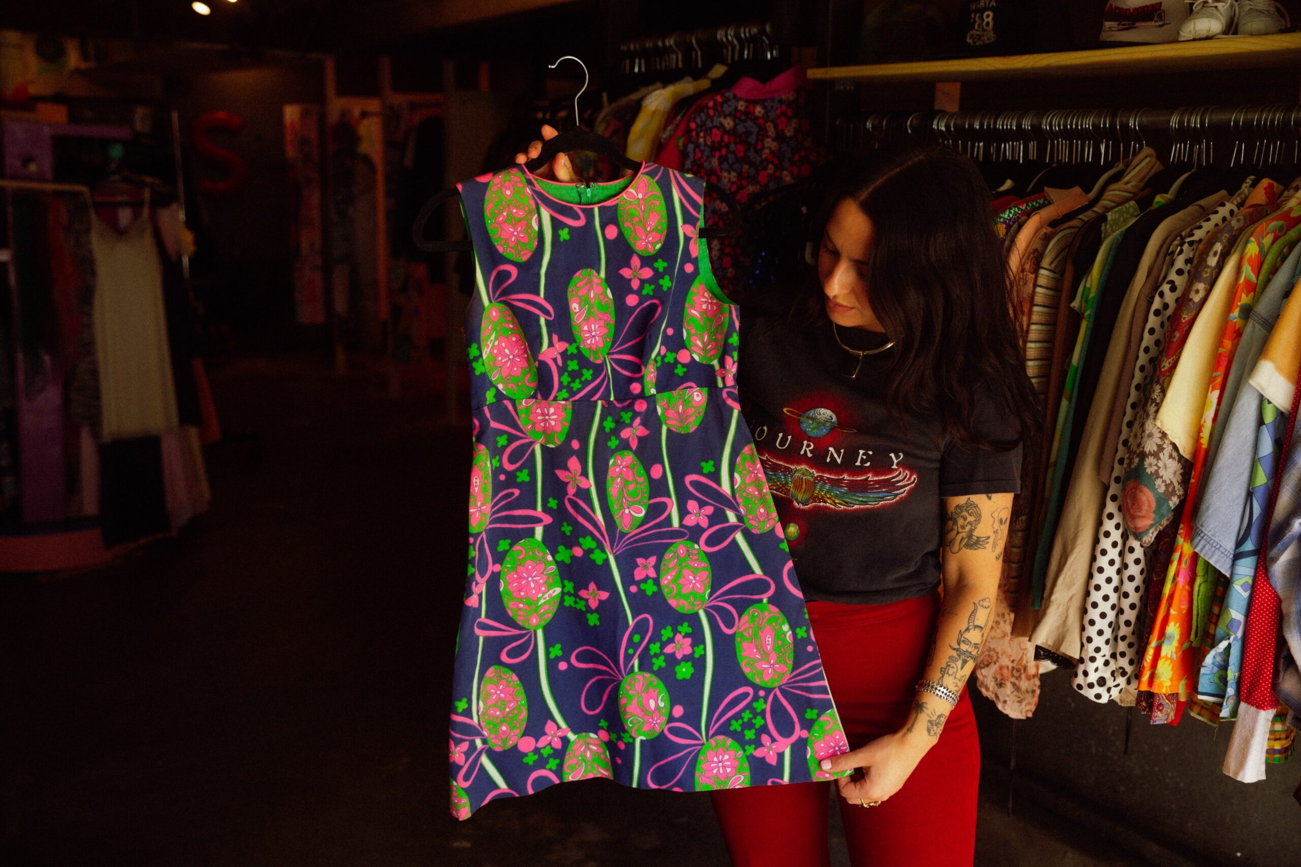 Sivan Peleg holds up a pink, green, and blue dress with a psychedelic pattern from the 1960s.