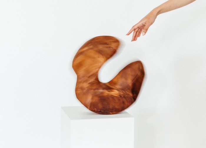 circular mahogany sculpture on the floor being rocked by a hand