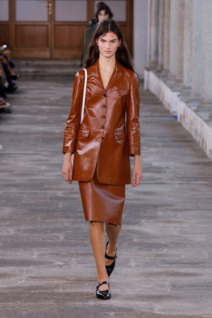 Female model on runway in brown leather coat and skirt