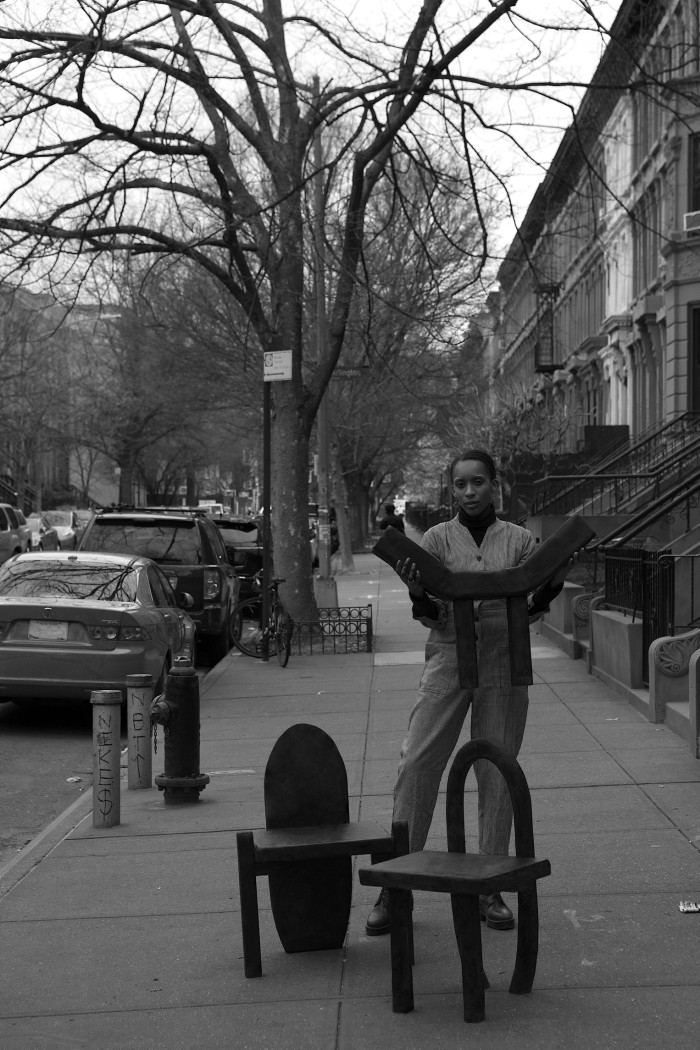 a woman standing in the street with chairs she has made