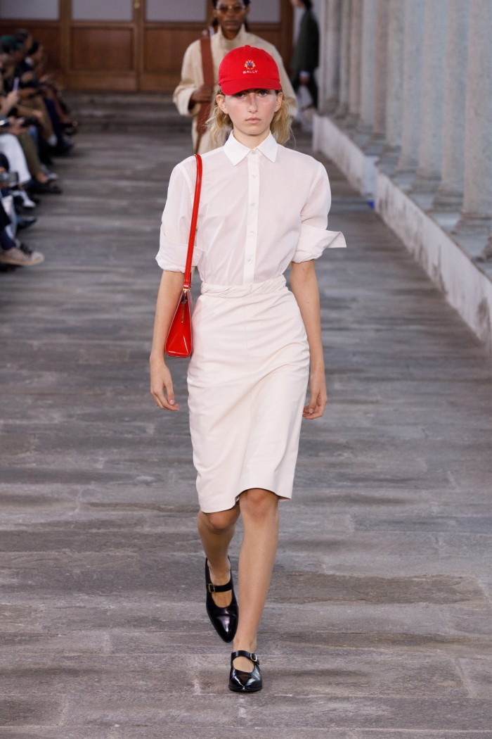 female model in white blouse and skirt and a red baseball cap