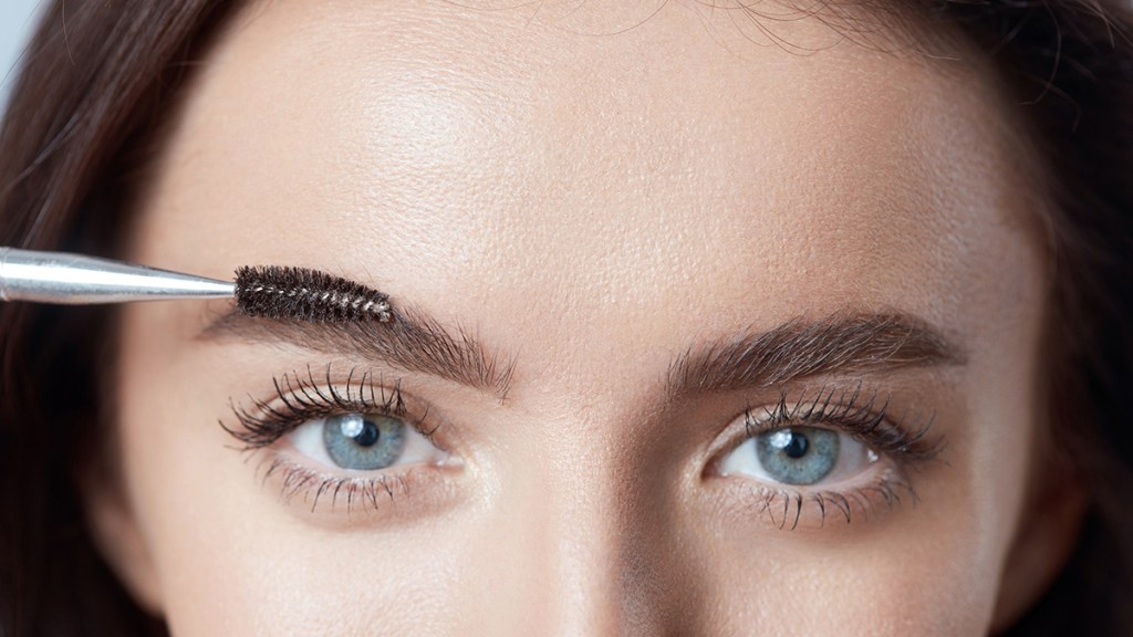 Woman brushing her eyebrows after applying a brow powder to create a similar effect to powder brows