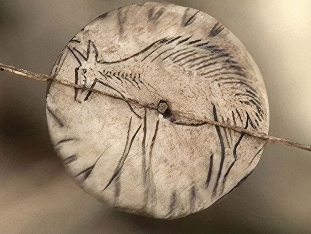 a small disk made of bone with animal etching spins on a string