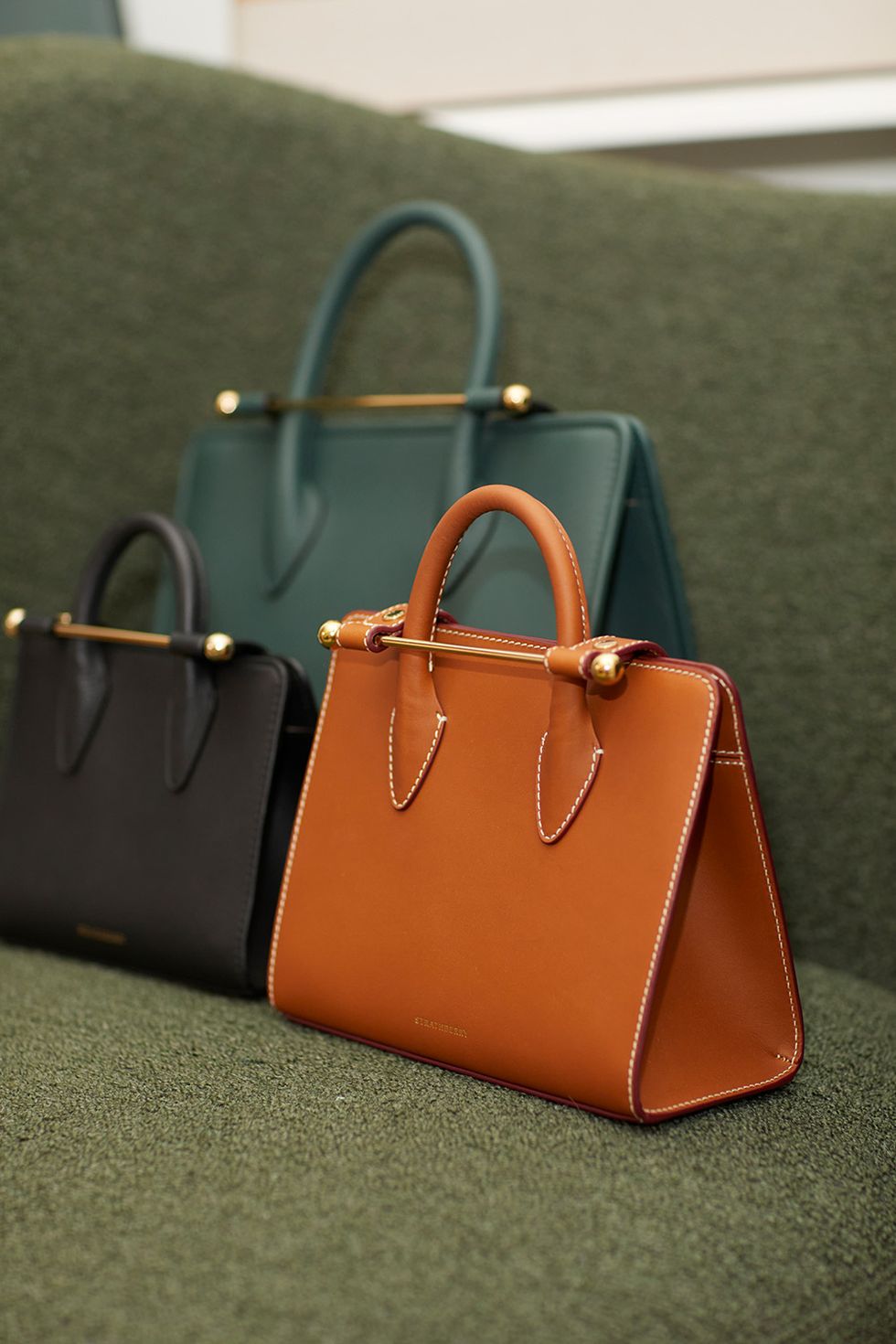 three strathberry bags in different colors sitting on a couch