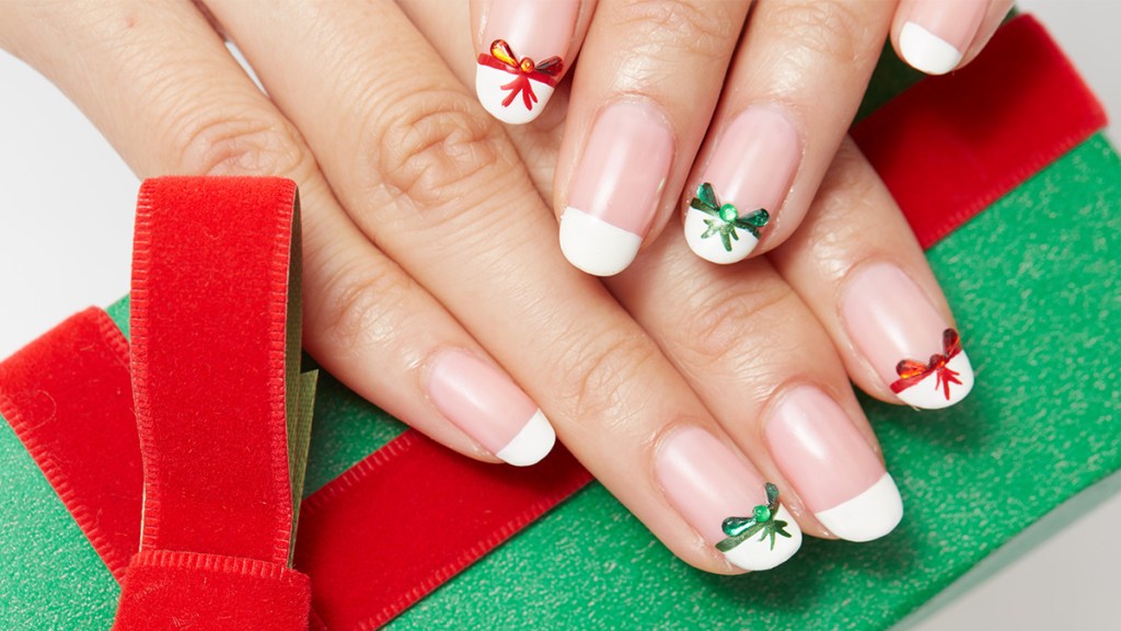 Nails painted with a French manicure that has red and green bows near the tips, one holiday nail ideas