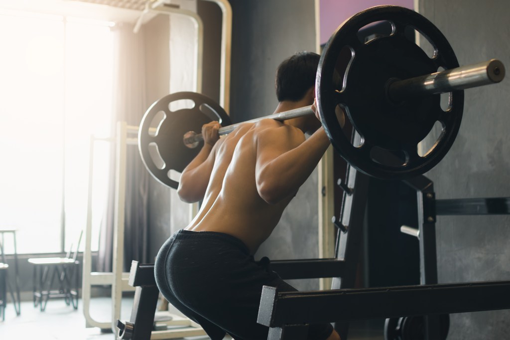 Rear view of asian man performing barbell squats