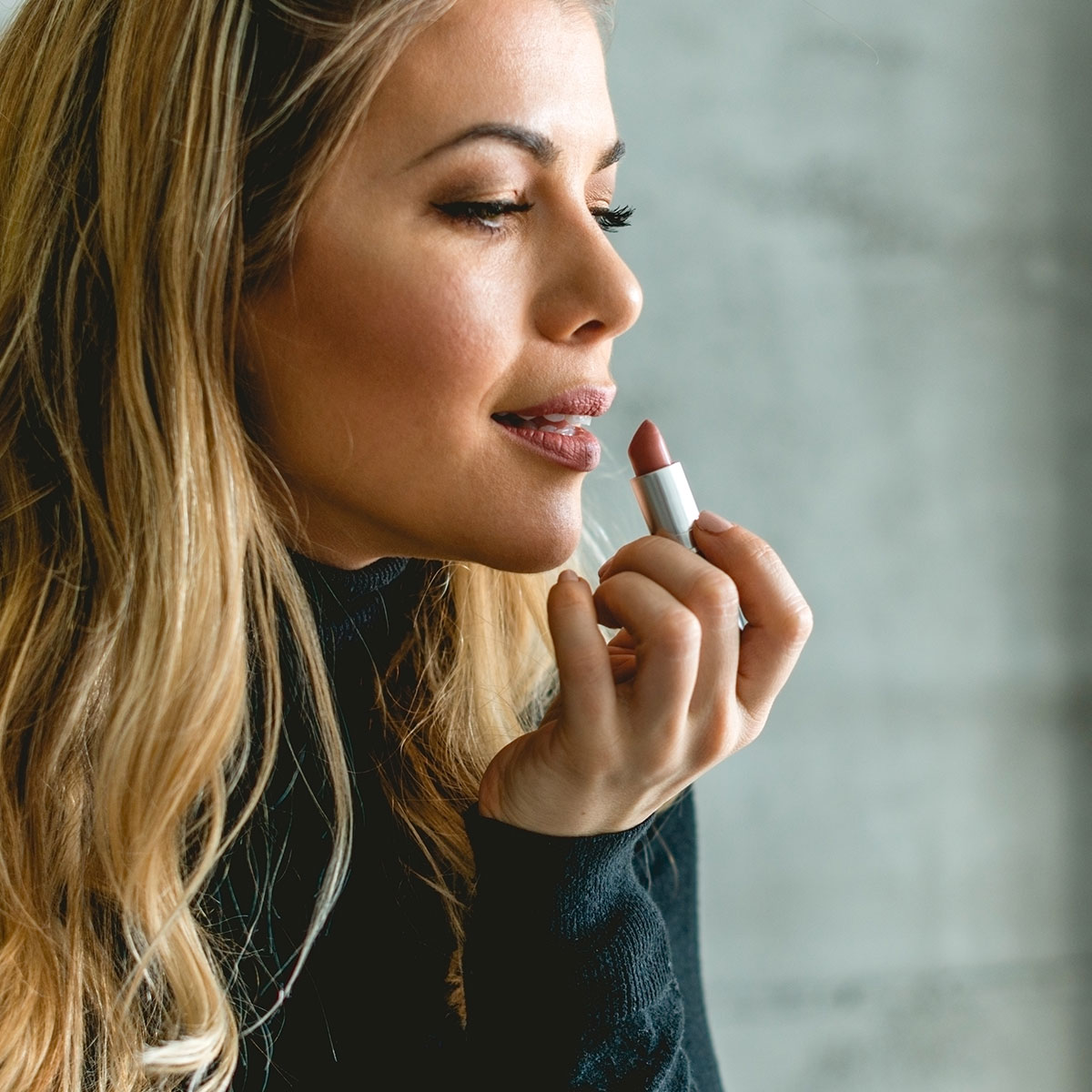 woman putting on lipstick while looking in mirror