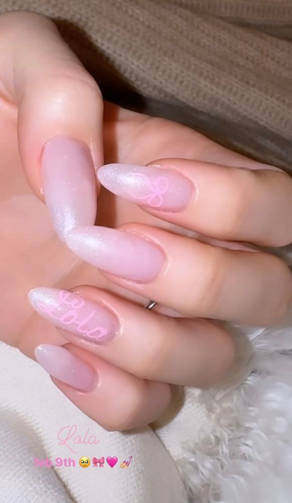 Nicola Peltz's pink shimmery nails with a bow on one finger and the word 