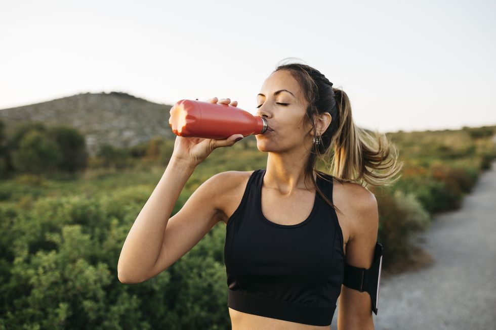 fit young woman in black sportswear drinking water from a reusable metal bottle after running workout