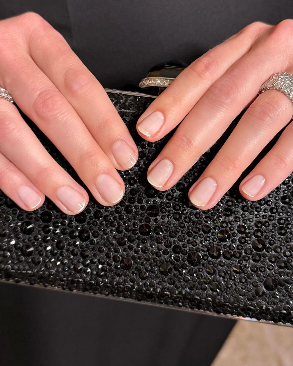 close of margot robbie hands showing a sheer pink manicure with just one thin line of white along the tip