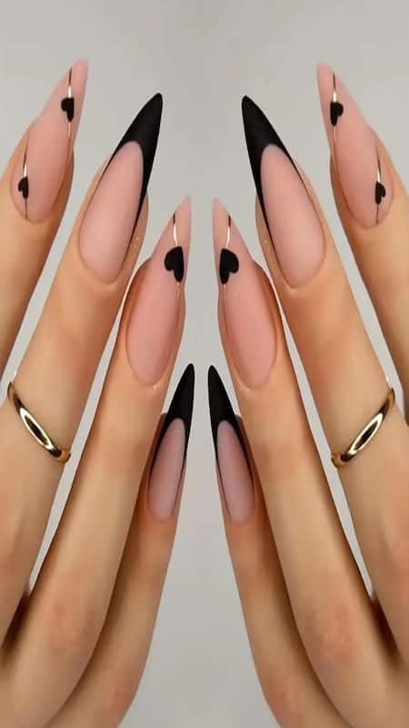 Chic Black Hearts: Sleek stiletto nails boasting a nude base with bold black tips, accented by delicate black hearts for a touch of elegance.