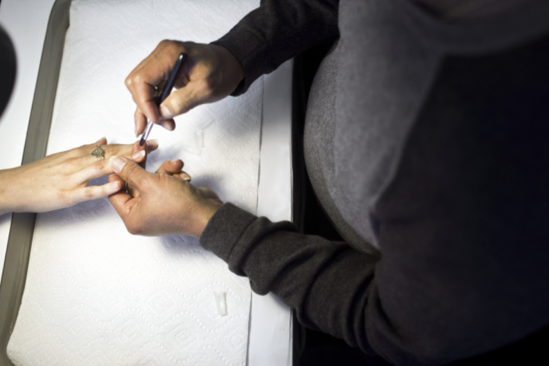 A male nail salon worker applies fake nails to a woman's hand.