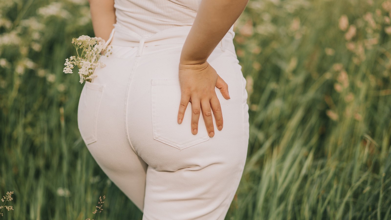 Closeup of a woman in white jeans on a blooming field background. Stylish look, fashion for curvy women, outdoor recreation.