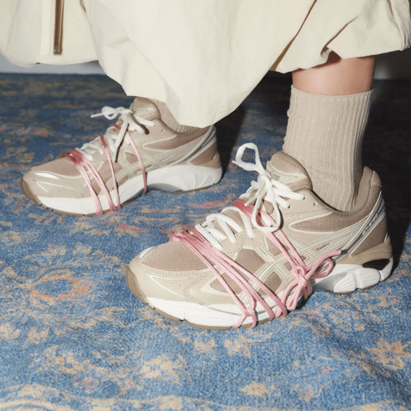 A model wearing chunky beige running shoes with light pink shoelaces tied around them