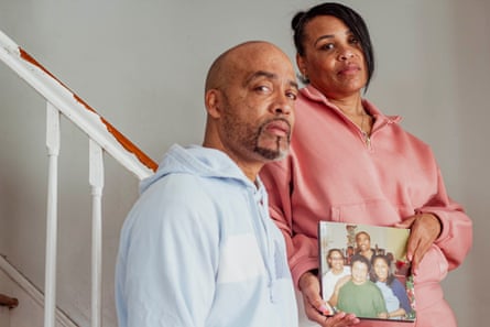 A man and a woman stand on a staircase holding a photograph of four smiling people.