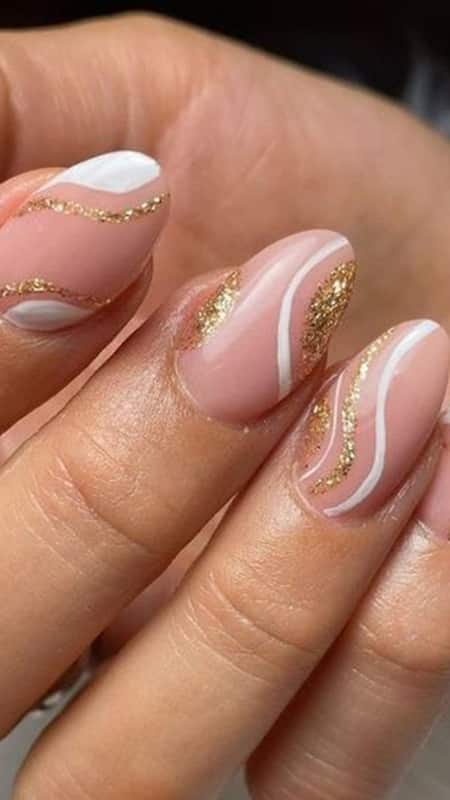 Sophisticated and playful, these nails feature a pale pink base with white and gold accents creating sleek swirls, perfect for a refined yet whimsical aesthetic.