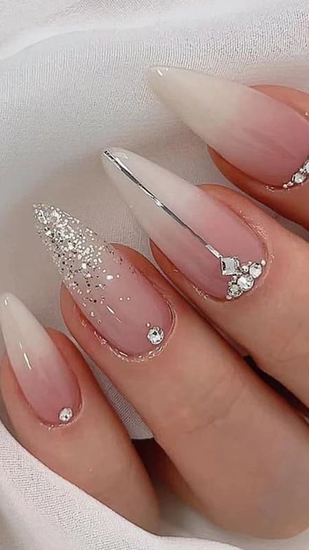 An elegant affair of stiletto nails, featuring a nude base, delicate rhinestone accents, and a sprinkle of glitter, blending classic charm with modern chic.