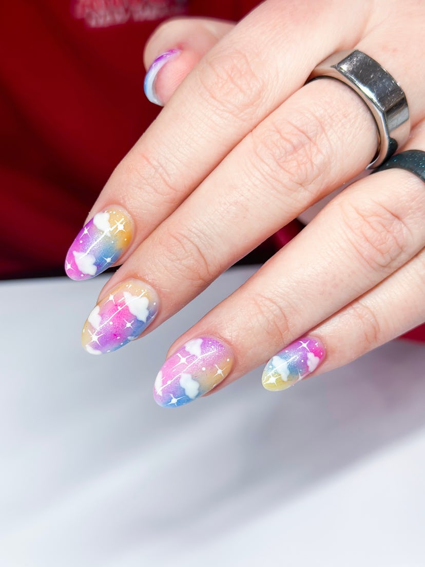 Hands with rainbow manicure with white clouds for Pride nails.