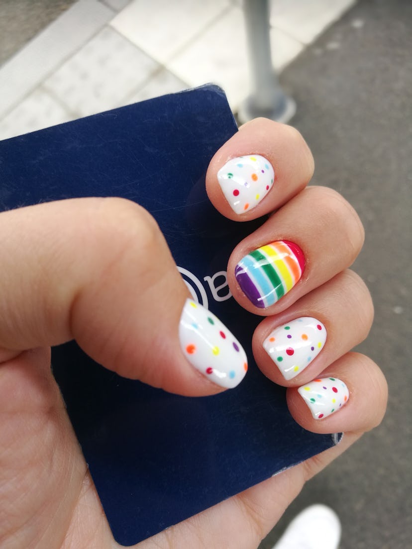 A hand with Pride nails in rainbow stripes and dots grasping a hotel key card.