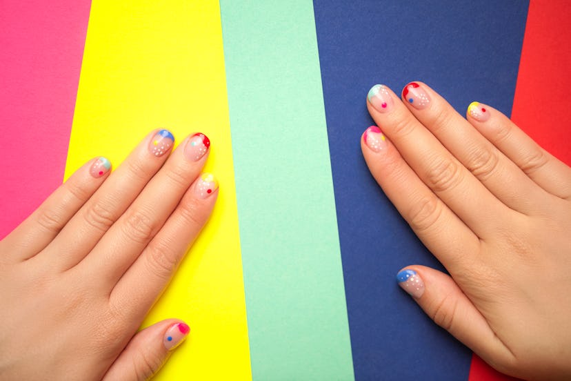 These pride nails feature a colorful French manicure are lying on bright multicolored background. 