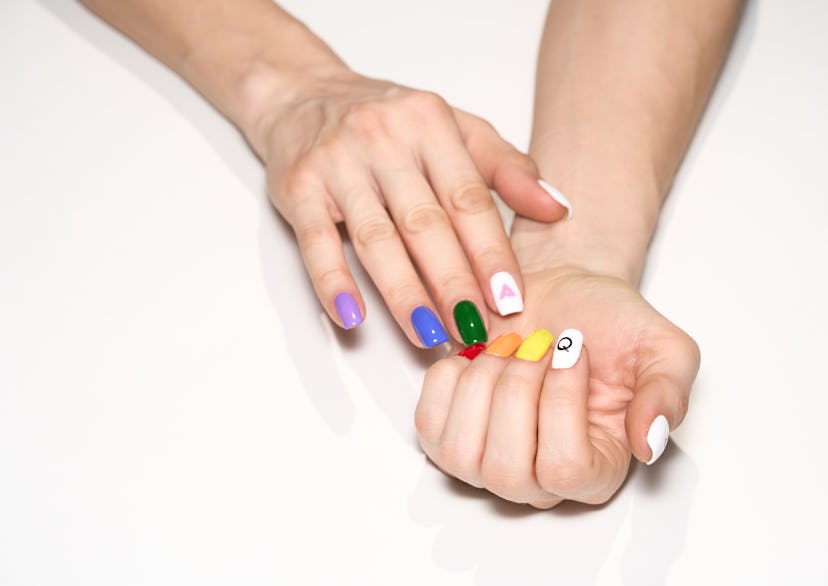 Hands with sporting Pride nails with rainbow colors and white nails with graphics.