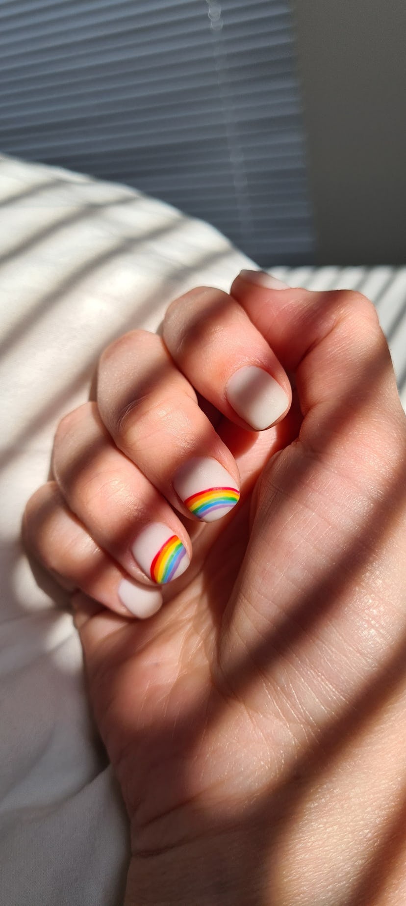 Nude-colored Pride nails with a subtle rainbow across the middle two nails.