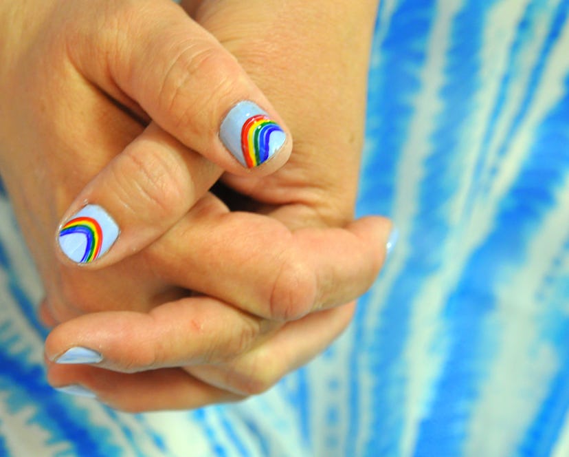 Two hands holdings with Pride nails decorated with rainbow colors on a light blue base.