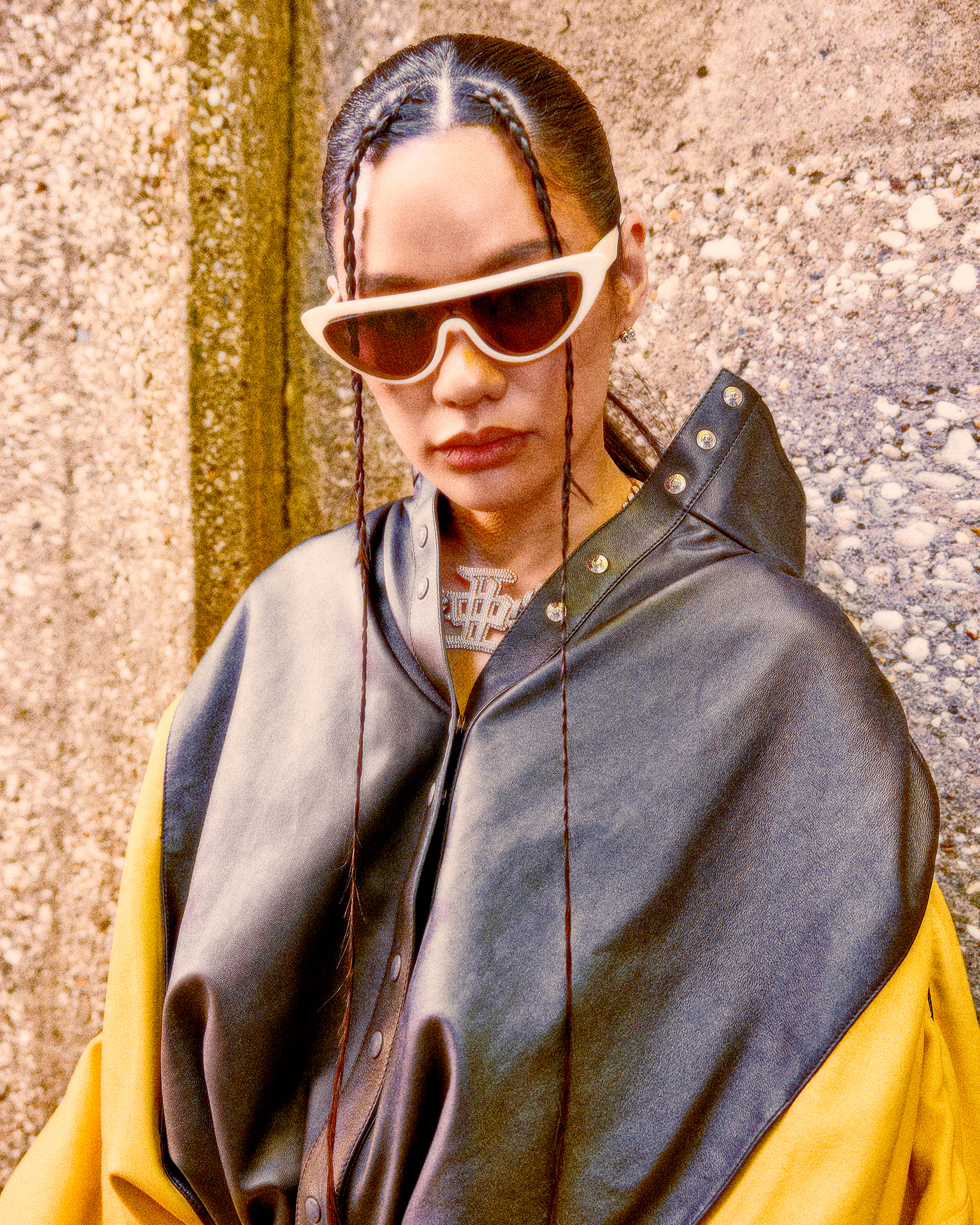 Japanese rapper AWICH, in a black and yellow jacket and white sunglasses, against a gray background.