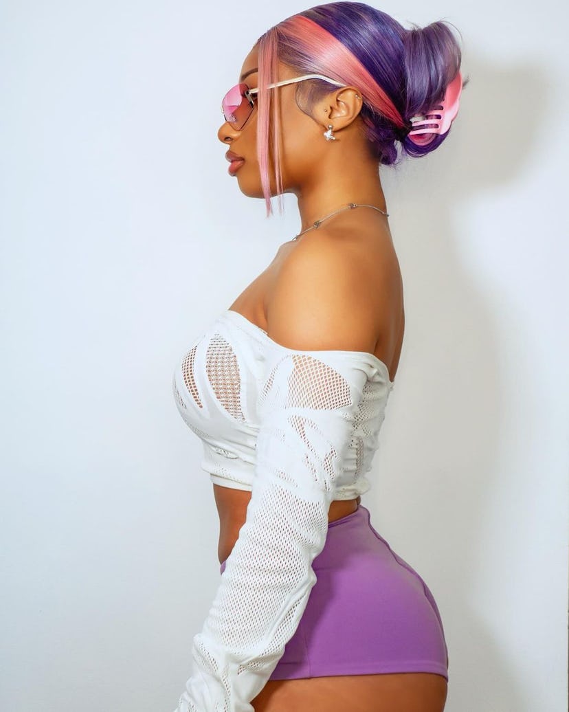 Megan Thee Stallion wears a sheer crop top and purple booty shorts.  