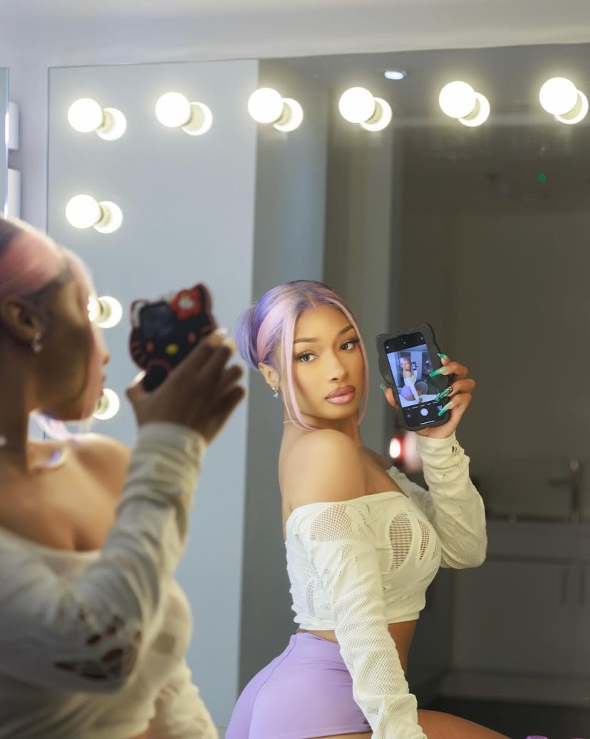 Megan Thee Stallion wears a sheer crop top and purple booty shorts.  