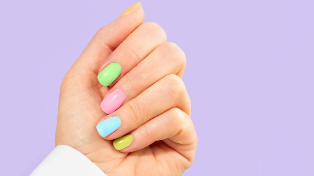 Elegant woman's hand with multi-color pastel manicure on Easter Holiday. Stylish trendy manicure. Woman dressed in fashionable white shirt. Trendy Color of the Year 2022 Very Peri purple violet lavender color background. Luxurious background design. Concept of Easter, Valentine's day. Front view. Copy space. Close-up.