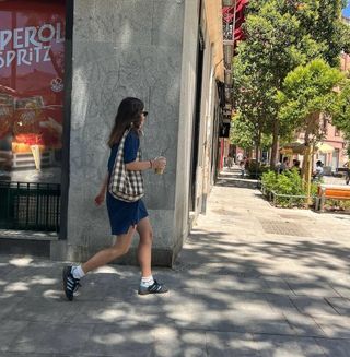 Woman wearing dark blue minidress, sling bag, and Adidas sneakers.