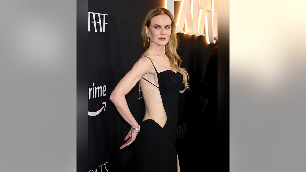 Nicole Kidman in a black dress puts her hand on her butt as she poses on the carpet