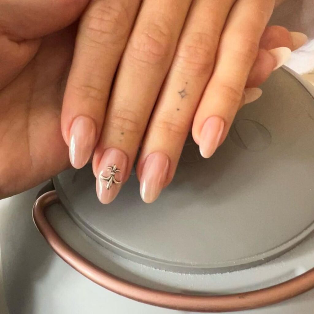 A nude almond shaped manicure with a single fleur de lis charm added to the middle nail. 