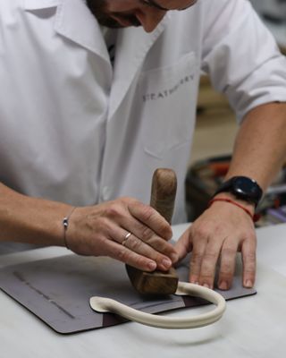 an artisan uses a wooden mallet to shape the handle of a strathberry handbag made in ubrique, spain