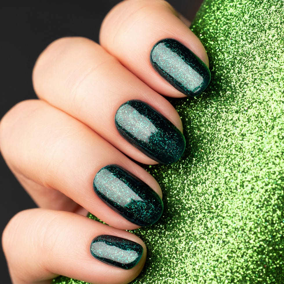 female hand with beautiful holiday manicure green glittered nails with glitter paper background with copy space selective focus nail care concept