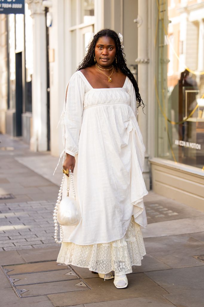 A guest wears white dress, laced skirt, round bag outside Bora Aksu during London Fashion Week September 2024 on September 13, 2024 in London, England