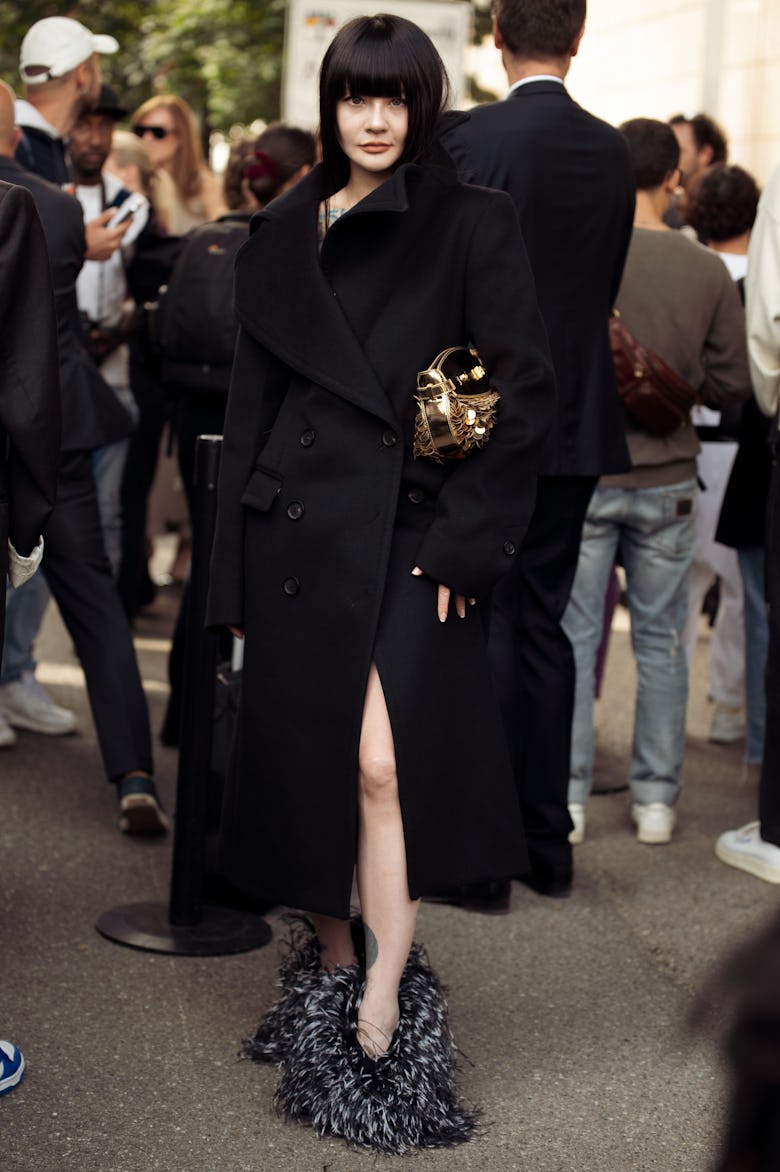 MILAN, ITALY - SEPTEMBER 21: A guest wears long black coat, grey fur shoes and golden bag outside Fe...