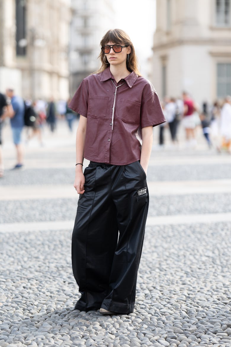 MILAN, ITALY - SEPTEMBER 22: A guest wears satin wide leg trousers, a silver necklace, silver hoop e...