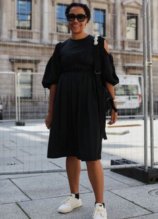 A woman in London dressed in a black dress and trainers