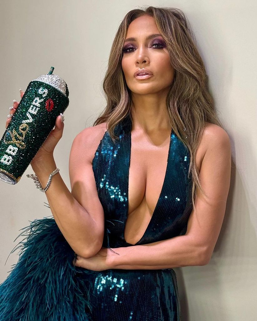 Jlo in a green emerald dress holding a sparkling cup 