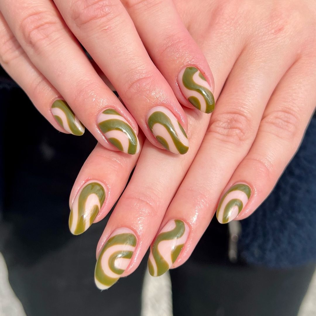 Almond nails with green and tan retro swirls on a clear base, creating a funky, vintage-inspired look that brings a playful touch to the classic manicure.