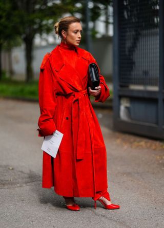 A guest wears gold earrings, bright red turtleneck long sleeve Ferragamo, bright red suede Ferragamo trench coat, bright red tight Ferragamo pants, shiny leather heels with strap, shiny black Ferragamo leather bag outside Ferragamo, during the Milan Fashion Week Spring/Summer 2024-2025 on September 21, 2024 in Milan, Italy.