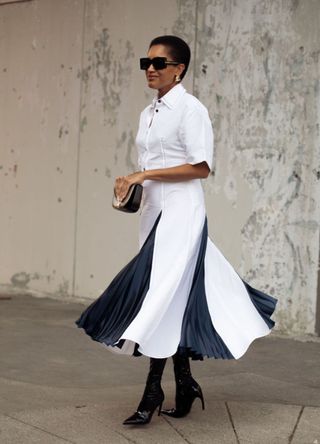 Tamu McPherson wears white and black 3/4 sleeve long dress, sunglasses, black bag or clutch and black pointy boots outside the Ferragamo show during the Milan Fashion Week Spring/Summer 2025 on September 21, 2024 in Milan, Italy.