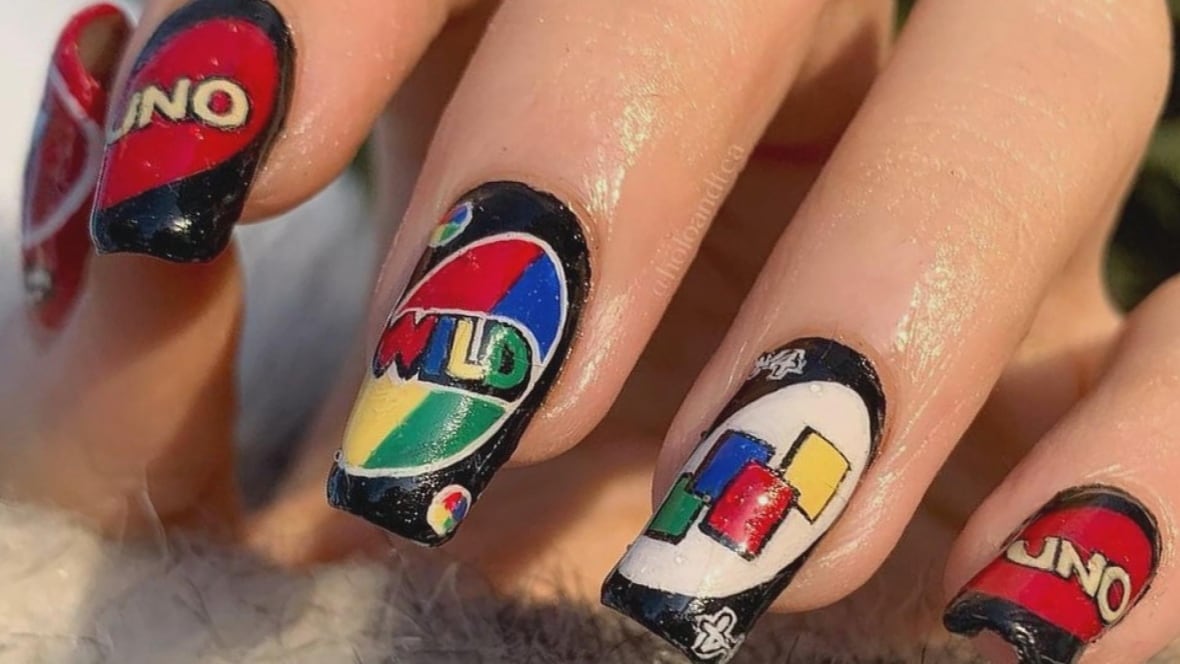 Long fingernails painted with Uno card game designs in bright red, black, white, blue, yellow and green. The Uno logo is on two nails. Another nail has 'wild' written across it; and a fourth nail has the pick up four cards design. 