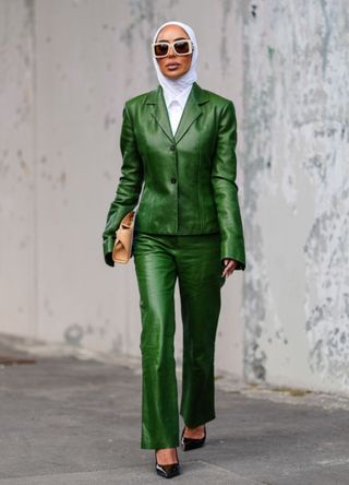 A guest wears white sunglasses, dark green leather jacket, dark green leather pants, light brown Ferragamo leather bag, shiny black pointed toe leather heels outside Ferragamo, during the Milan Fashion Week Spring/Summer 2024-2025 on September 21, 2024 in Milan, Italy