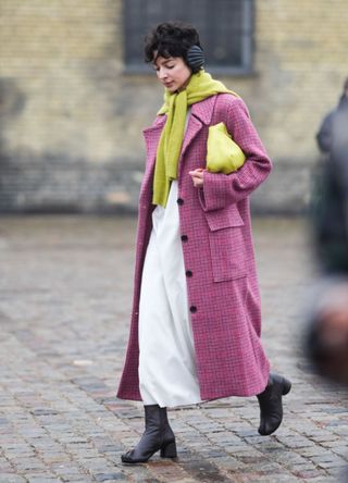 A guest wears a yellow wool pullover worn as a scarf, a red / pink checkered / checked pattern printed long coat, a yellow leather bag, outside Rolf Ekroth, during the Copenhagen Fashion Week AW24 on January 30, 2024 i